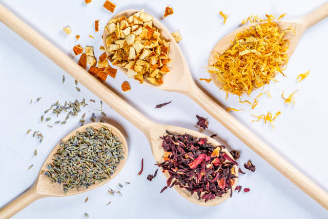 Holzlöffel mit getrocknetem Tee aus Lavendel, Hibiskus, getrockneter Orangenschale und Blüten