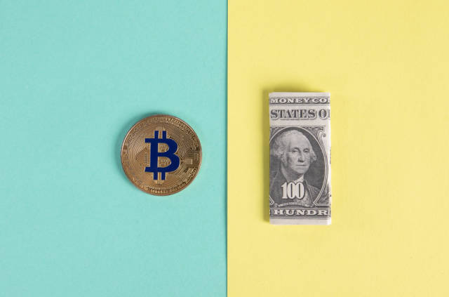 Golden Bitcoin coin and folded one hundred dollar banknote