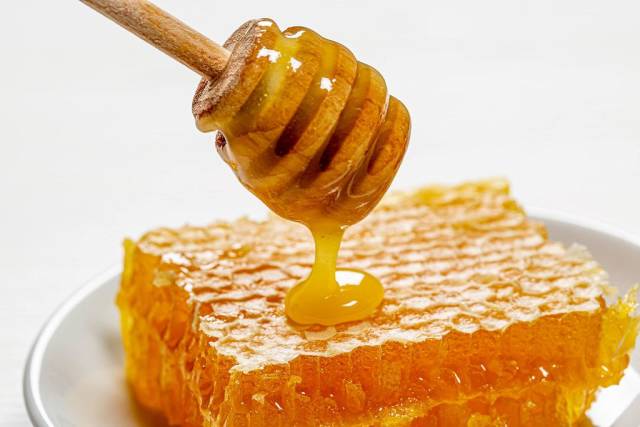 Tropfender Honig auf-Honig-Waben und weißem Teller