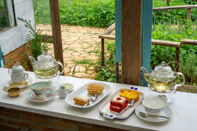 Glass Tea Pots, Tea Cups,  Plates and other Ceramics on a Wooden Windowsill facing a Garden