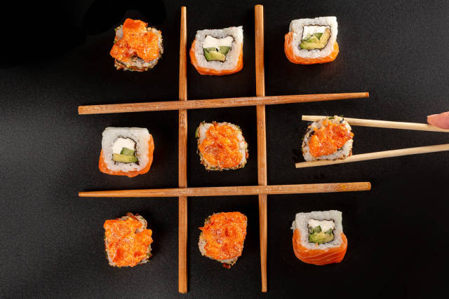 Tic-tac-toe game concept, sushi with chopsticks on black background