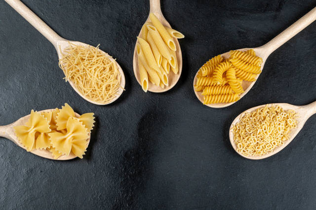 Top view, food concept-different shapes of pasta in wooden spoons