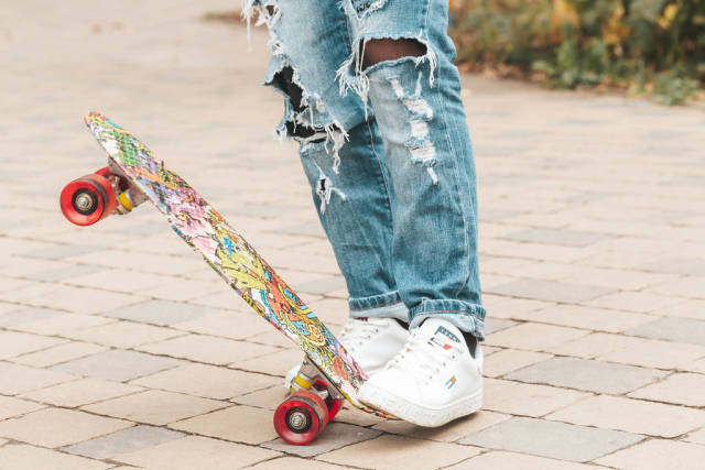 Legs of a girl in ripped jeans with a skateboard