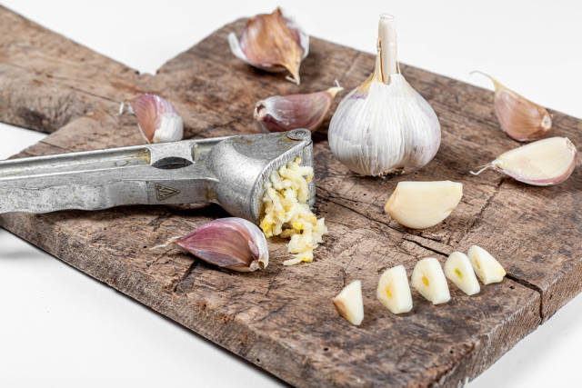 Bulbs of garlic on old cutting board, garlic press and cloves of garlic
