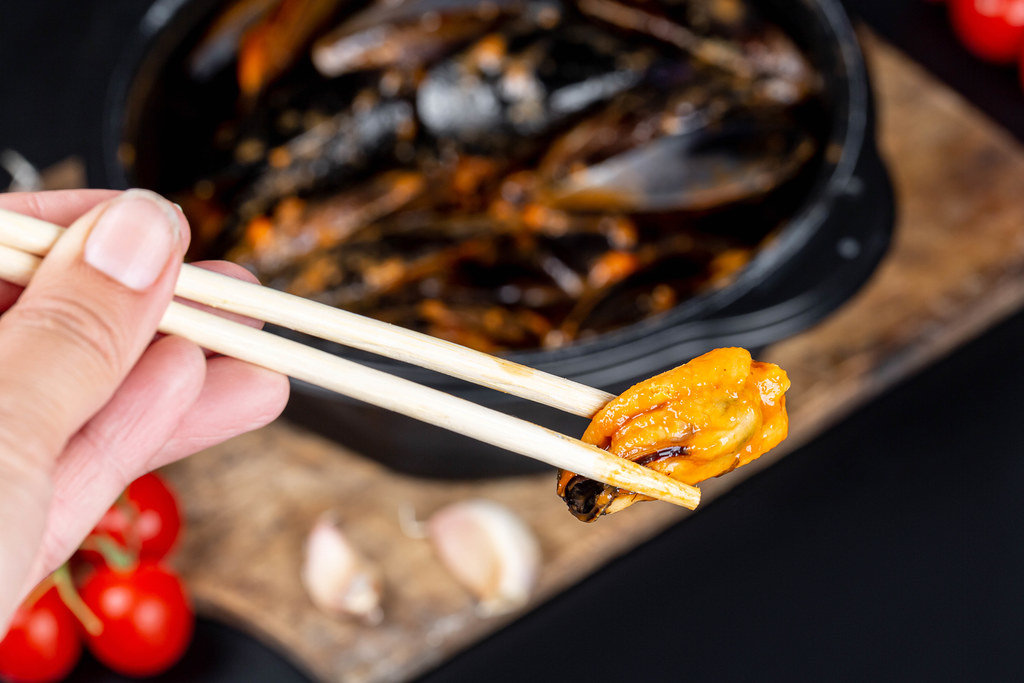Chopsticks with mussels in a womans hand