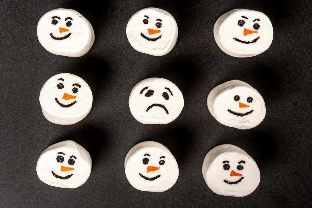 Top view, funny marshmallow emoticons and one sad on black background