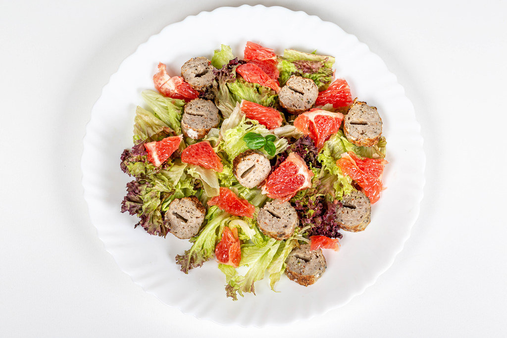 Salad with lettuce, grapefruit and grilled sausage, top view