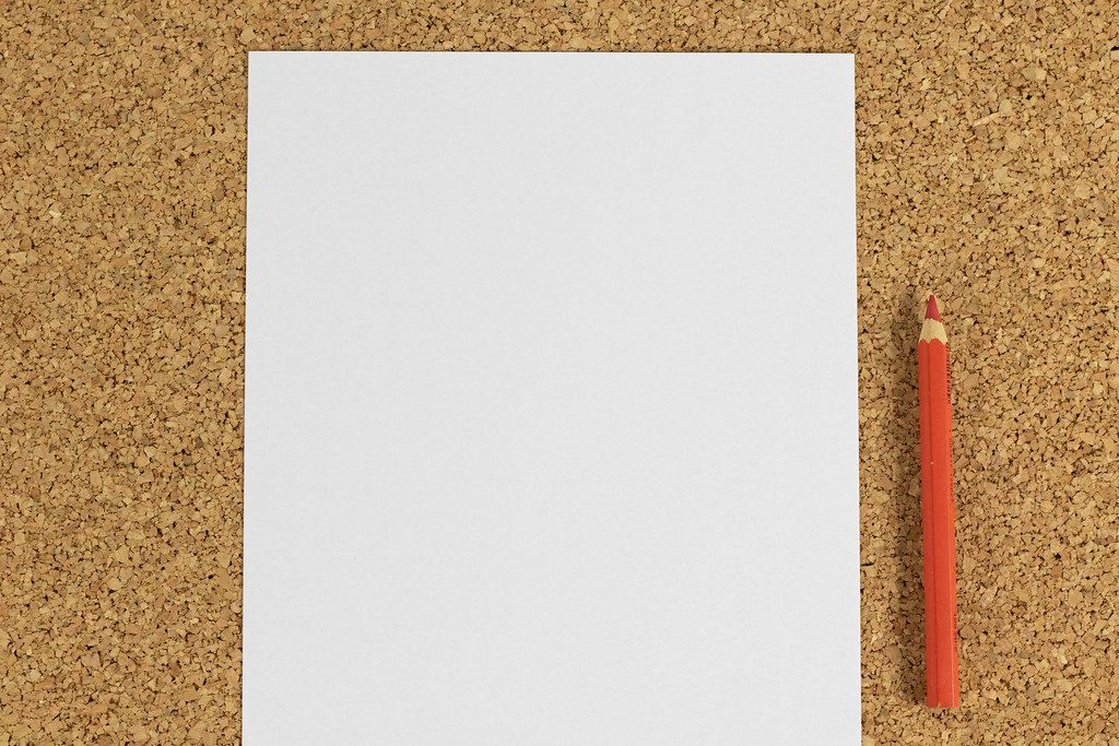 Weißes Blatt Papier mit rotem Bleistift auf einer Oberfläche aus Korken