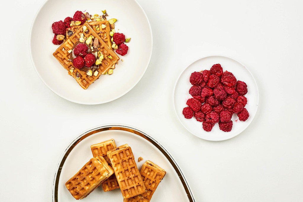 Belgian waffles with raspberries for tasty breakfast on white table