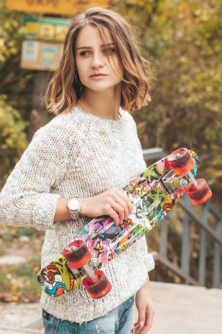 Close up of young attractive girl with skateboard standing outdoors and looking away