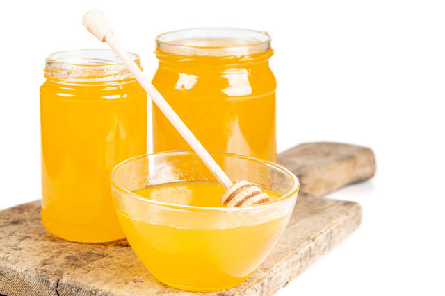 Bee honey in glass jars and a bowl with a wooden honey dipper