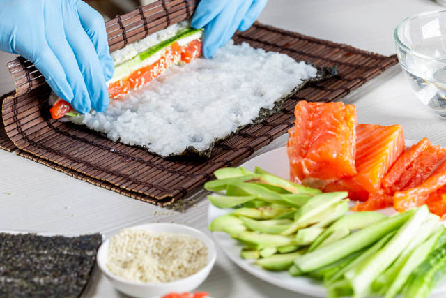 Cook preparing sushi with salmon and avocado