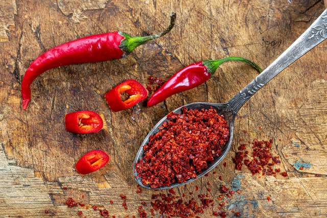 Hot red chili peppers and red pepper flakes in spoon on old wooden background