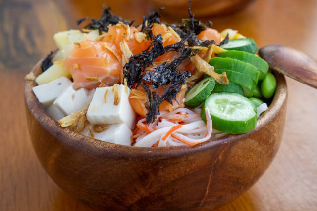 Close Up Food Photo of Wooden Bowl with Hawaiian Dish Poke Bowl with Surimi, Tofu, Fried Onions, Dried Seaweed, Vegetables and Raw Salmon