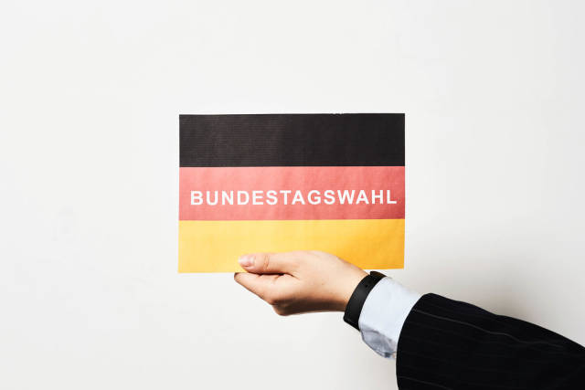 Hand eines Mannes mit Anzug und Hemd hält eine deutsche Flagge mit Schrift "Bundestagswahl