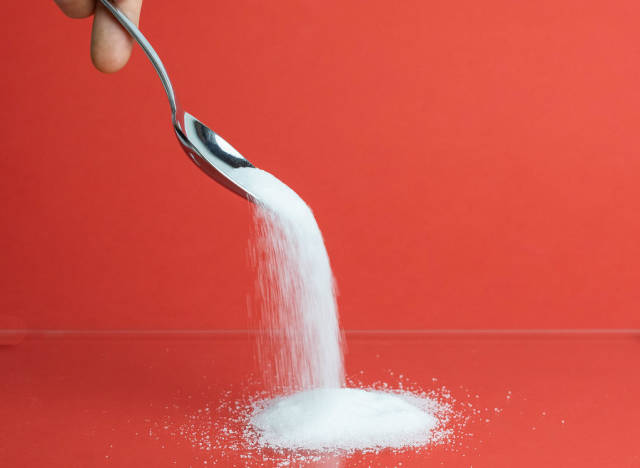 Weißer Zucker rieselt von einem Löffel auf rotem Hintergrund
