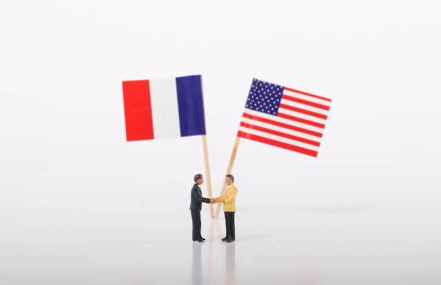 Two businessman shaking hands in front of flags of France and USA