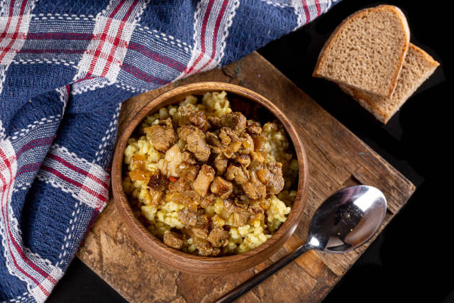 Top view, bowl of porridge with meat on old wooden kitchen board