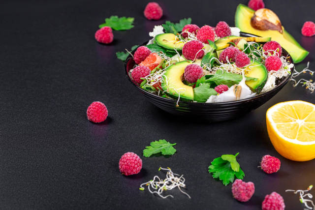 Vegetable salad with avocado, greens, onion micro-greens and raspberries on a black background