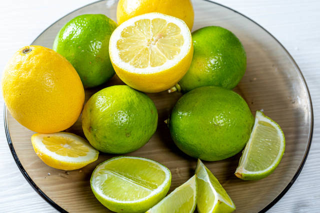 Fresh lemons and limes whole and pieces on a glass black plate