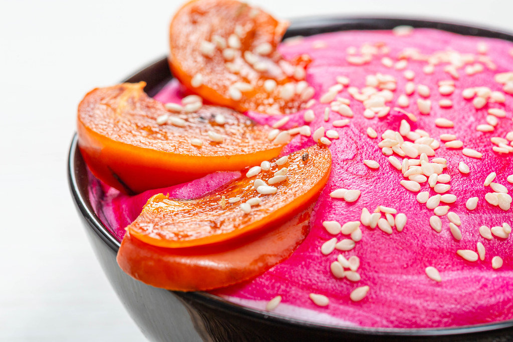 Close-up of slices of persimmon and sesame seeds on pink yogurt. Beautiful oatmeal for Breakfast