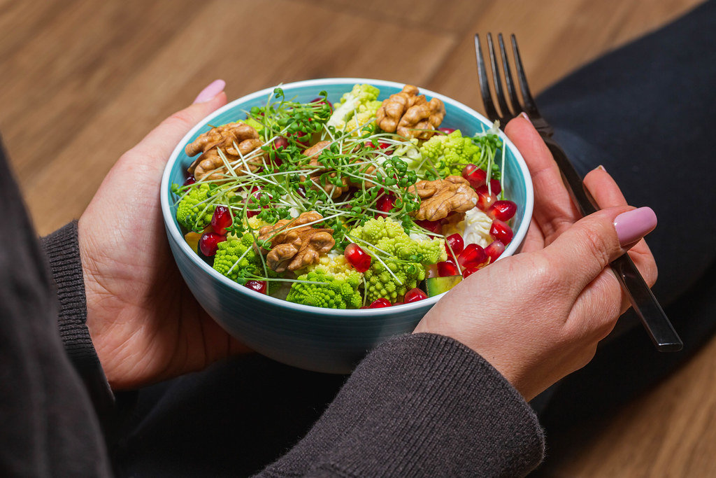 Close-up of a vegetable salad with nuts and micro greenery in a womans hands with a black fork. Dietary food