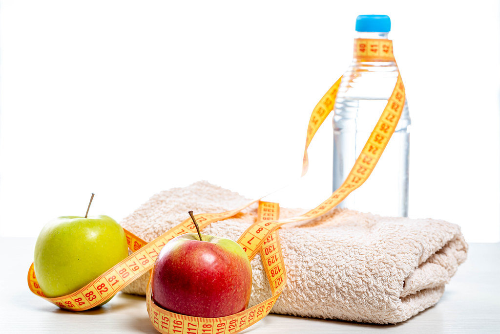Measuring tape wraps around a bottle of clean water, apples and a towel. Sports concept, healthy lifestyle