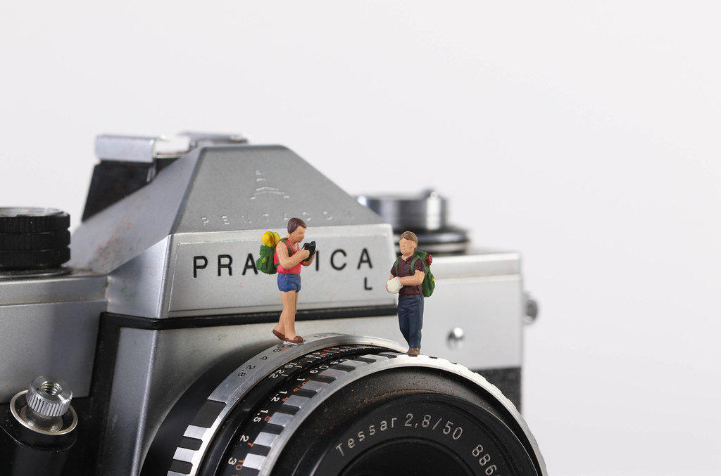 Miniature travelers standing on vintage camera