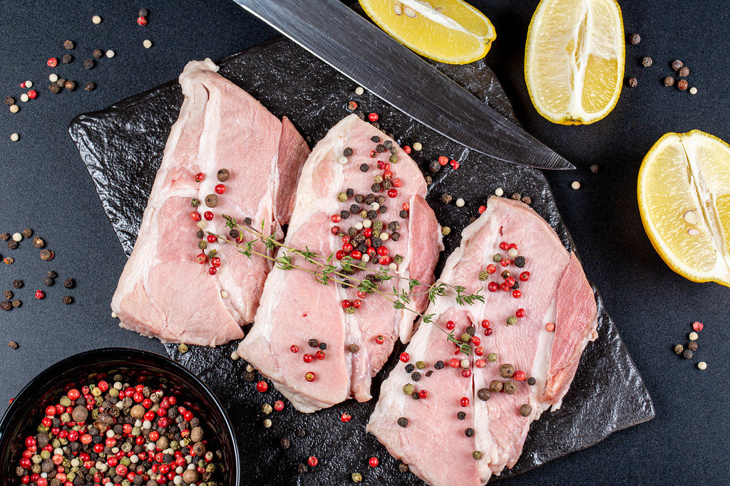 Top view, steaks with spices, lemon slices and a knife on a dark background