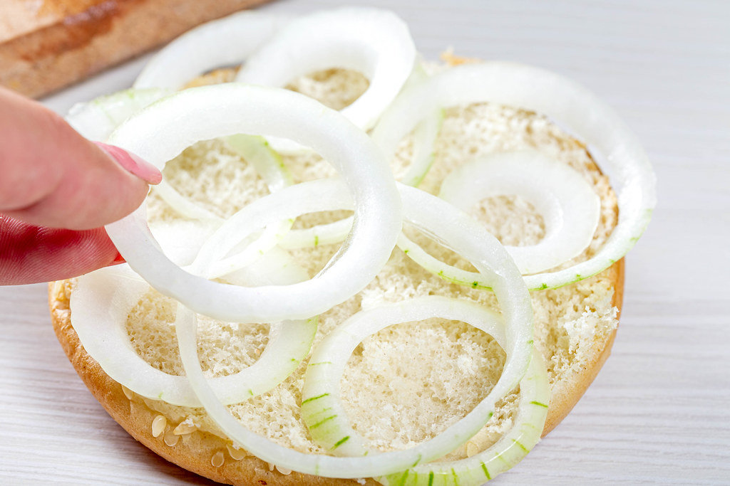 Womans hand puts onion rings on half of hamburger bun