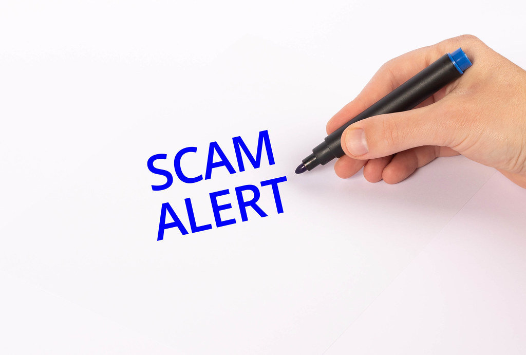 Hand with blue marker writing Scam alert text