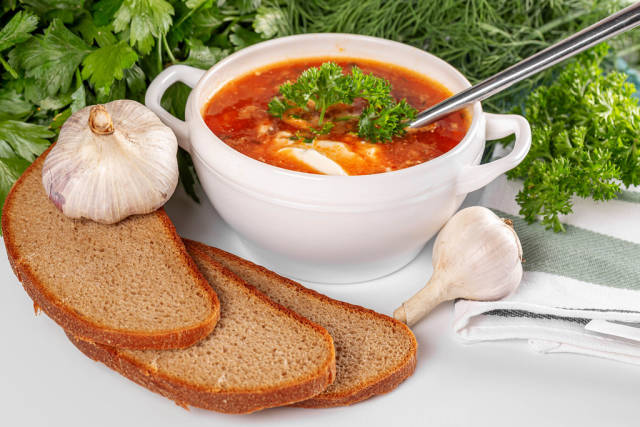 A bowl of borscht with sour cream, black bread, fresh garlic, dill and parsley