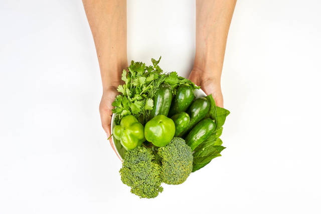 A woman holds fresh green vegetables for detox salad