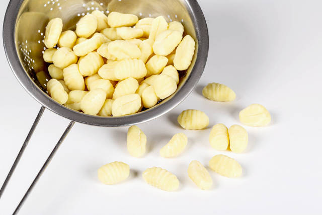 Potato gnocchi in colander on white background