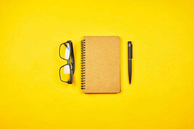 A writers workspace. Notepad with eyeglasses on yellow background