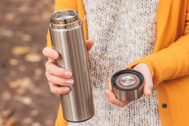 Girl holding an open thermos in her hands outdoors