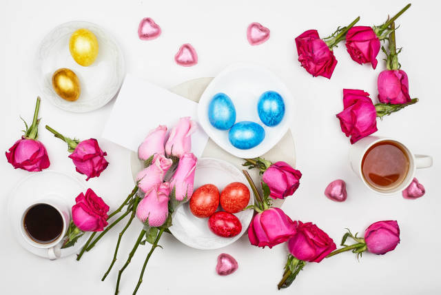 Romantischer Hintergrund zu Ostern mit bunten Eiern, Rosen, Kaffee und Schokoherzen