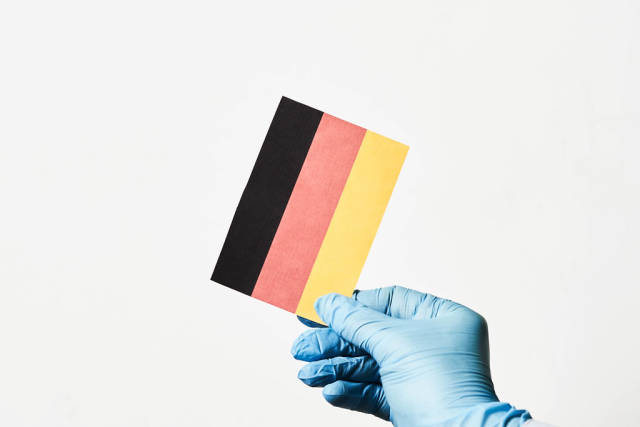 Covid-19 in Deutschland. Hand mit Einmalhandschuh hält eine deutsche Flagge vor weißem Hintergrund