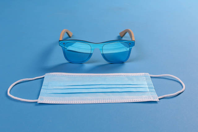 Sunglasses and medical face mask on blue background