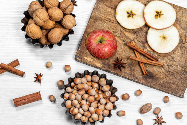 Hazelnuts, walnuts, cinnamon sticks, anise and apples on white wooden background