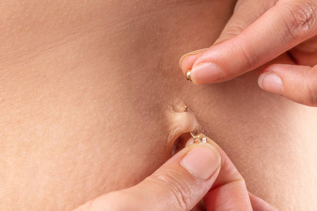 Womans hands putting on her navel piercing