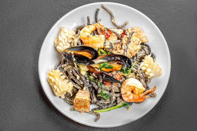 Top view noodles with cuttlefish ink in creamy sauce with seafood