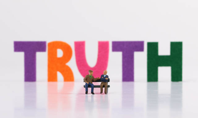 The word Truth with two seniors sitting on bench on white background