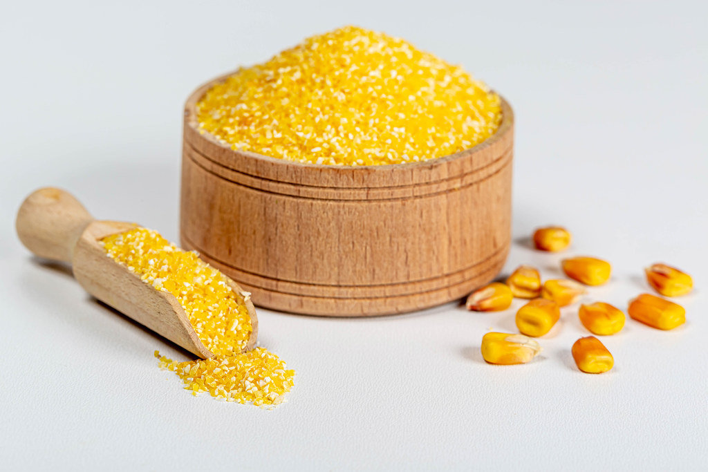 Raw corn grits in a wooden bowl and scoop on a white background