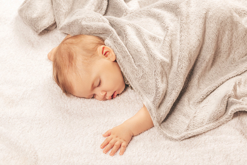 Sweetly sleeping baby covered with a gray blanket