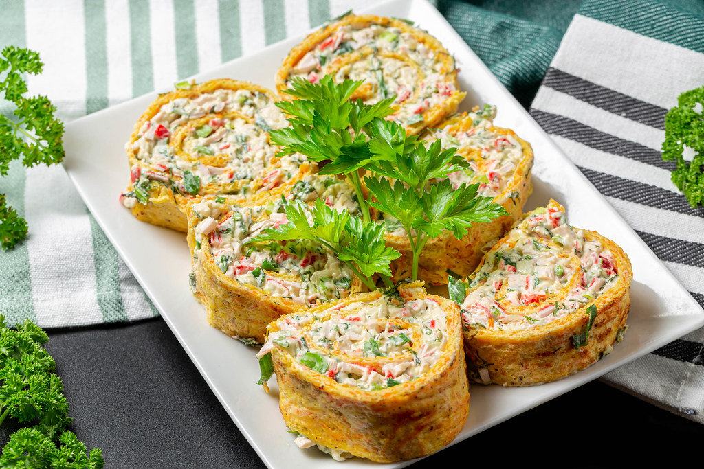 Sliced cheese omelette roll with herbs and crab sticks on a white plate