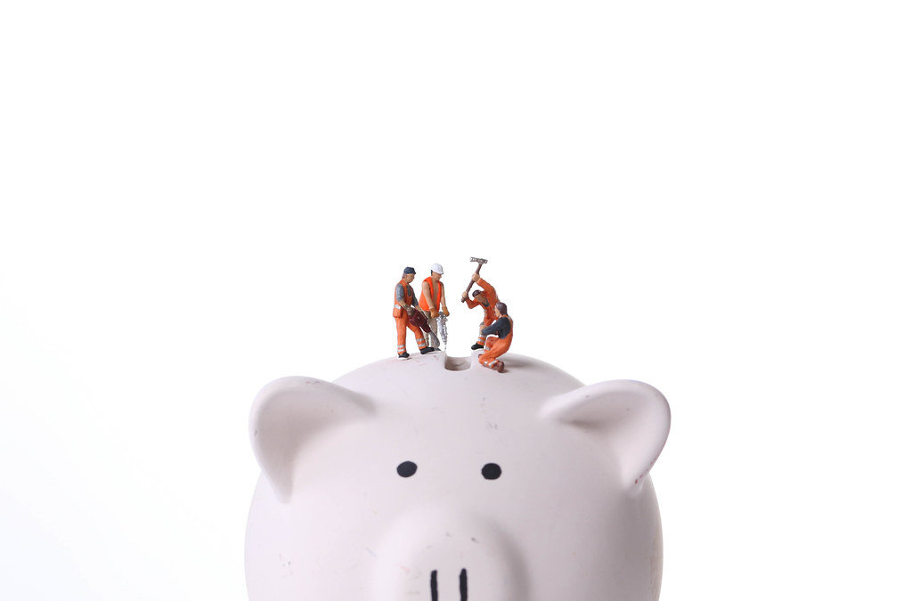 Group of miniature workers on top of piggy bank