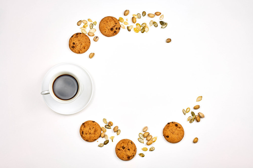 Black coffee, sweet oatmeal cookies, and different nuts forming a half-circle on white