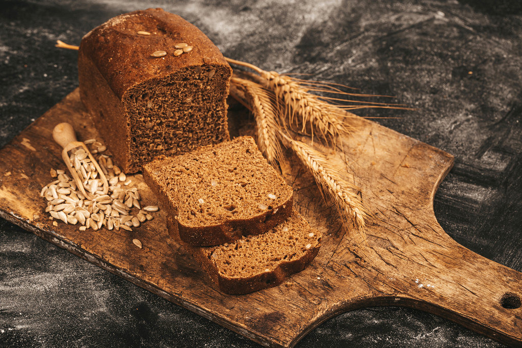 Sliced black bread with sunflower seeds and wheat ears on a dark background