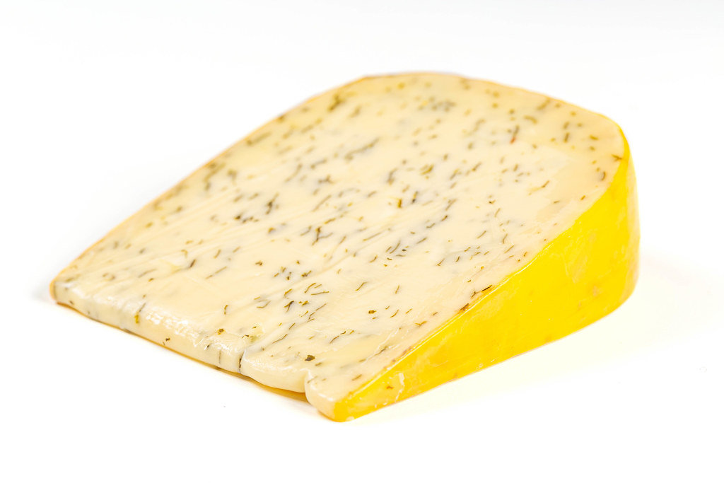 A piece of Dutch cheese with herbs and garlic on a white background
